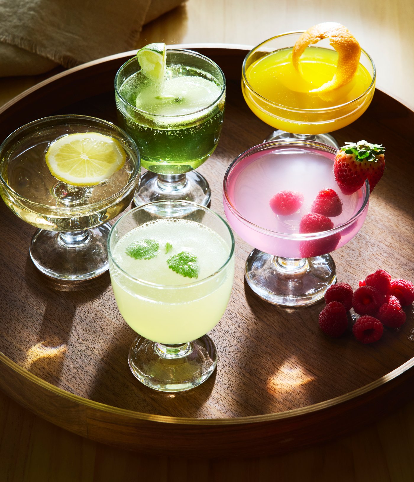 Two FRUKTDUVA goblets and three FRUKTDUVA champagne coupes filled with various drinks stand on an OMBONAD tray.