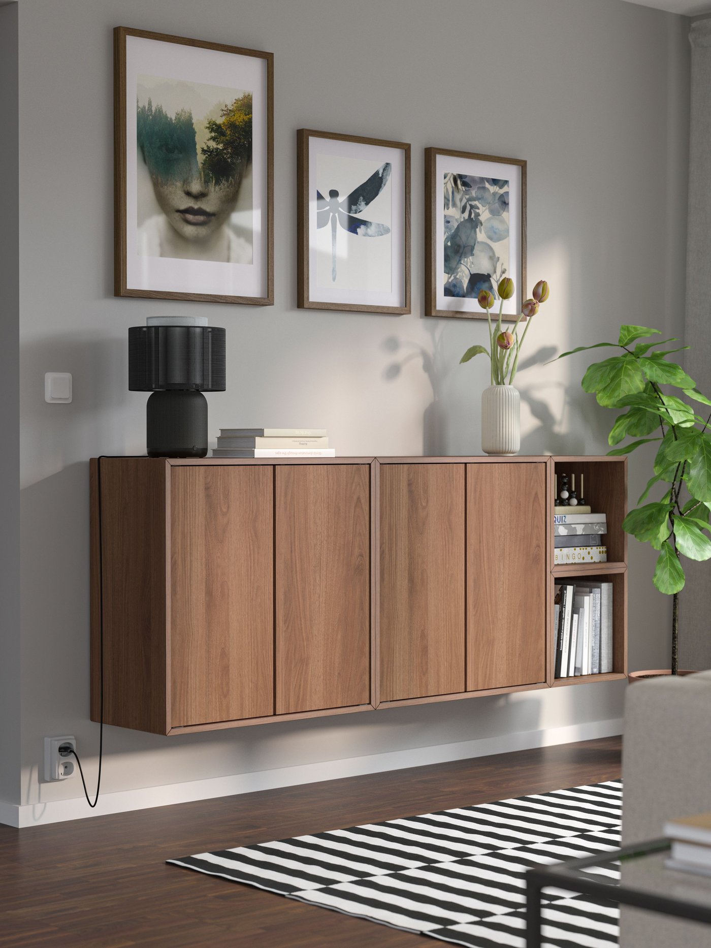 Ett vägghängt lågt skåp i valnöt med 5 dörrar hängande på grå vägg med tre tavlor ovanför. 