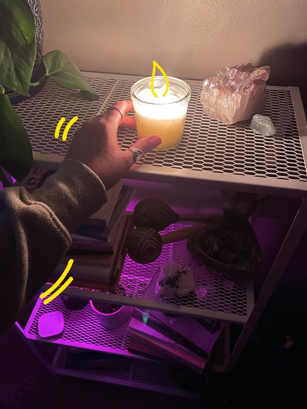 A hand placing a JÄMLIK candle on top of a metal shelf next to crystals.
