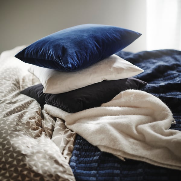 Close-up of a pile of different dark blue and white pillows on top of bed with a blue SKOGSKOVALL bedspread.