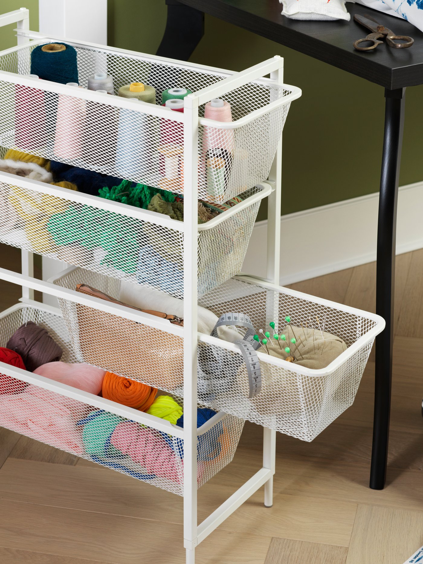 Espacio de trabajo con una combinación de módulos de almacenaje blancos, accesorios de costura, objetos personales, unas tijeras, un escritorio negro y tela.