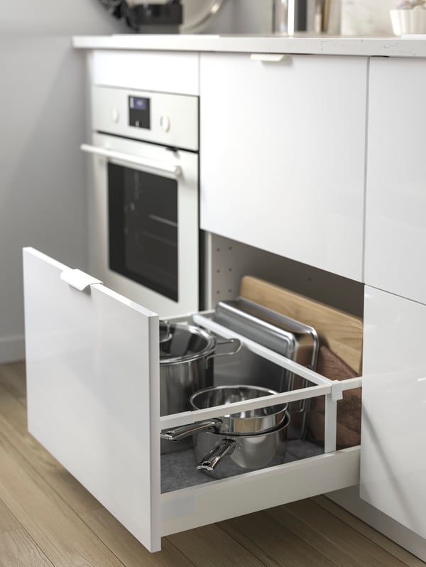 Four IKEA RINGHULT white glossy kitchen drawers. One is open to reveal pots and other kitchen utensils stored inside.