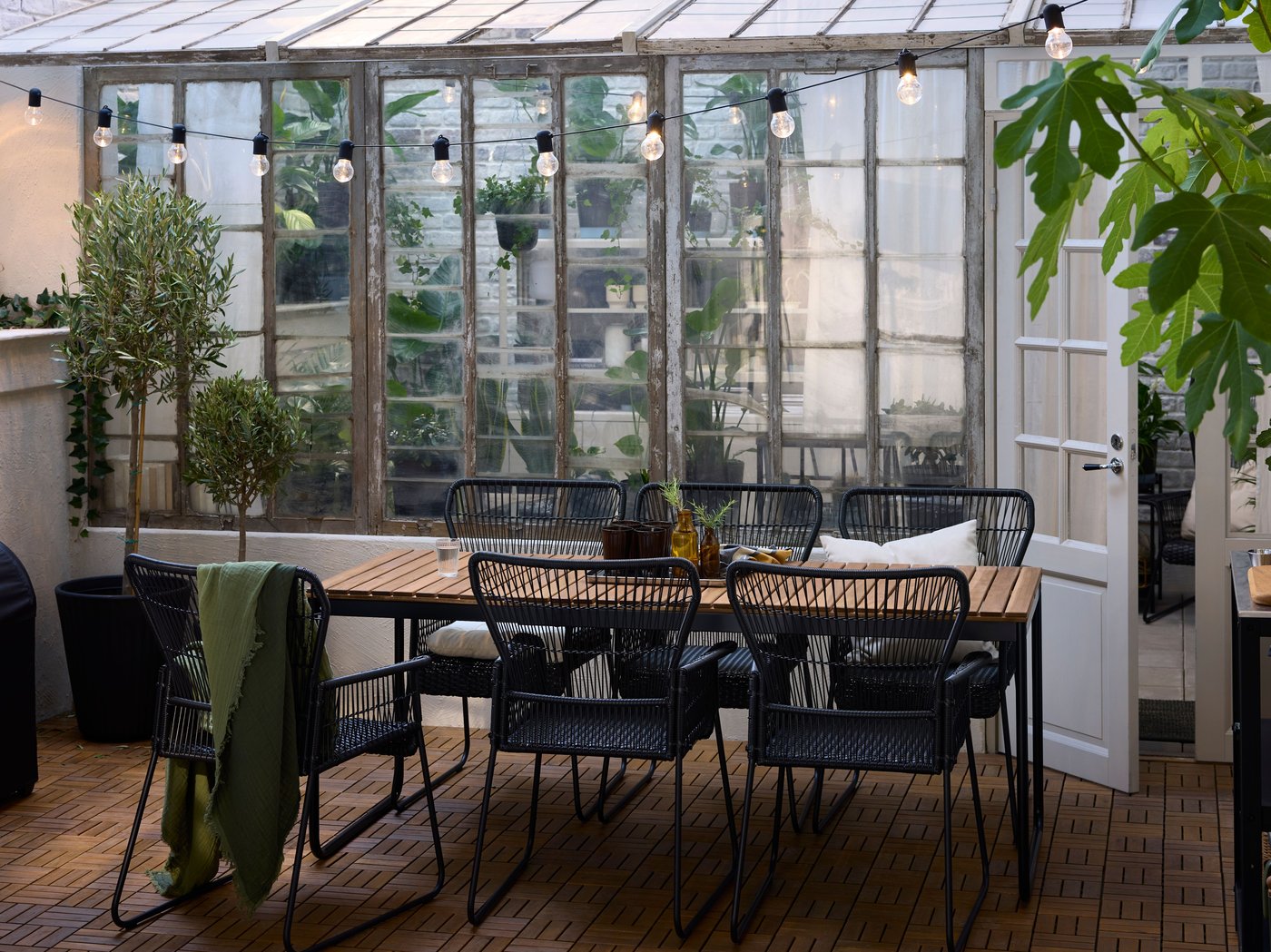 A backyard with a VÄSMAN extendable table and TALLSKÄR outdoor chairs with armrests on an acacia outdoor floor decking.