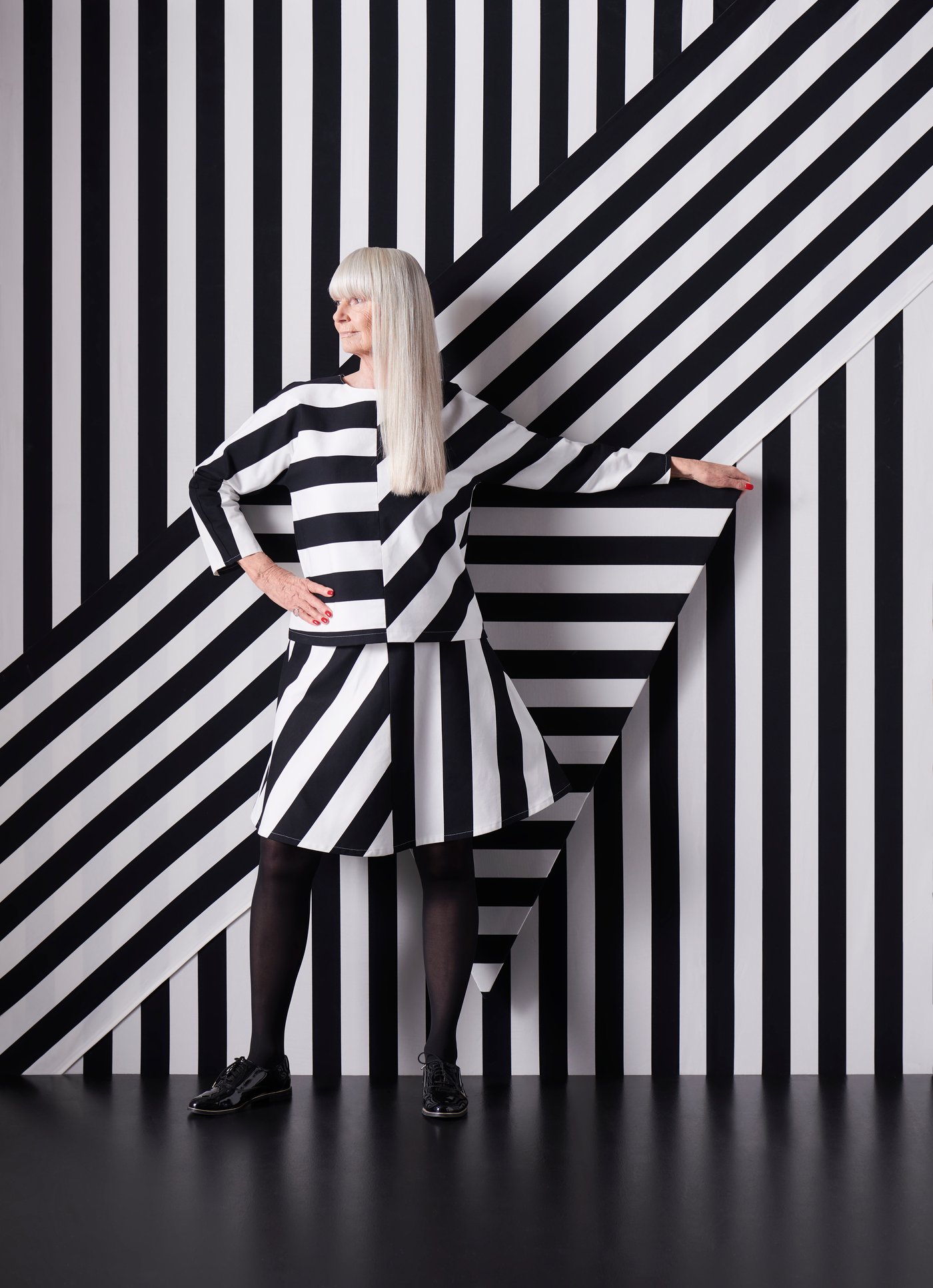 امرأة ترتدي فستانًا مصنوعًا من قماش SOFIA مخطط بالأبيض والأسود تقف أمام جدار مغطى بنفس القماش.