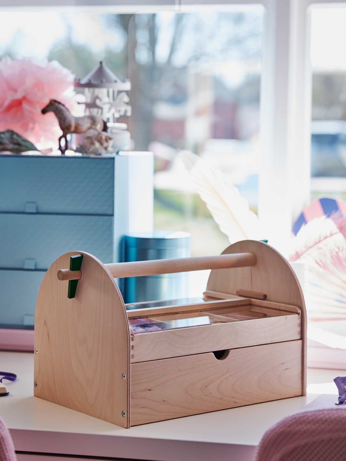 A wooden LUSTIGT arts and crafts storage sits on a table by a window in front of a PALLRA mini chest with 3 drawers.