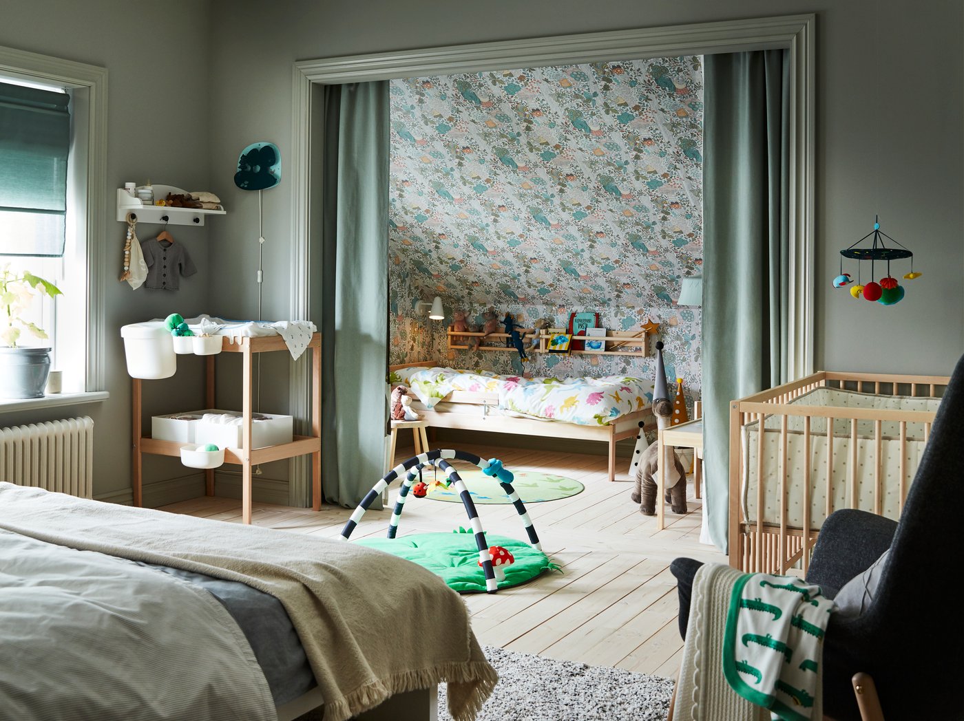 Bedroom with a double bed, a changing table and baby accessories. A children’s bed stands in an alcove behind green curtains.