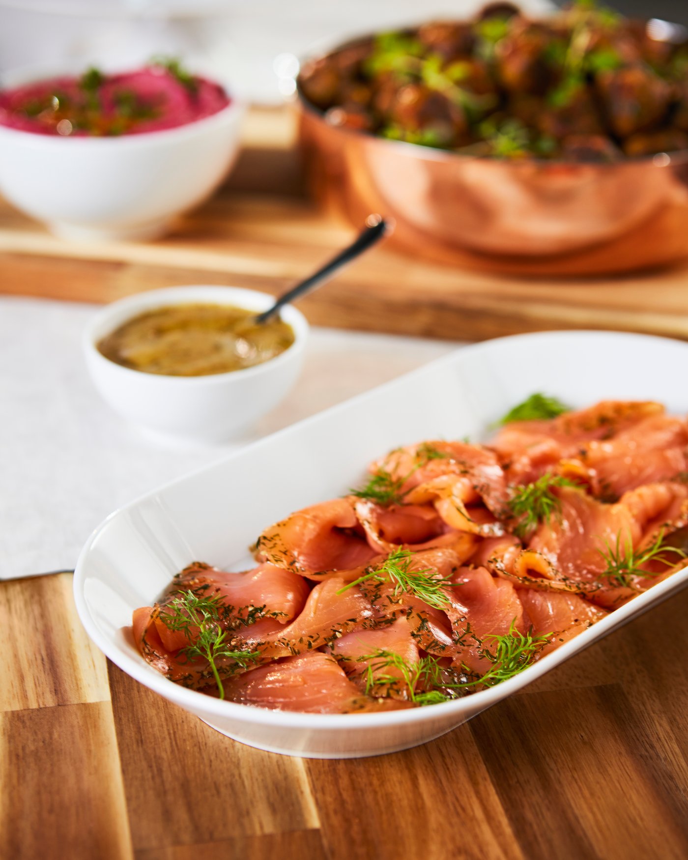 Una tavola con un piatto di salmone marinato SJÖRAPPORT con dietro una salsa di senape aromatica e altre portate. 