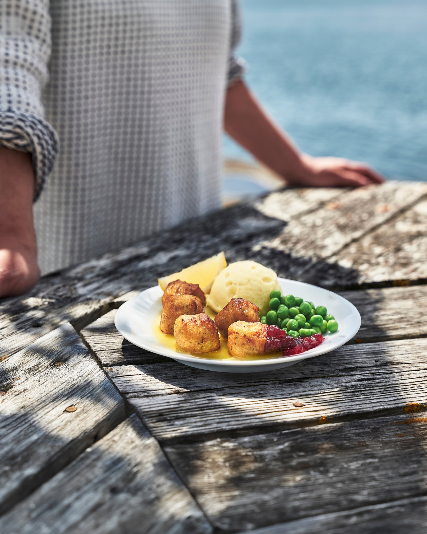 Fried and crunchy fish balls with mashed potatoes and green peas, butter and cranberries.