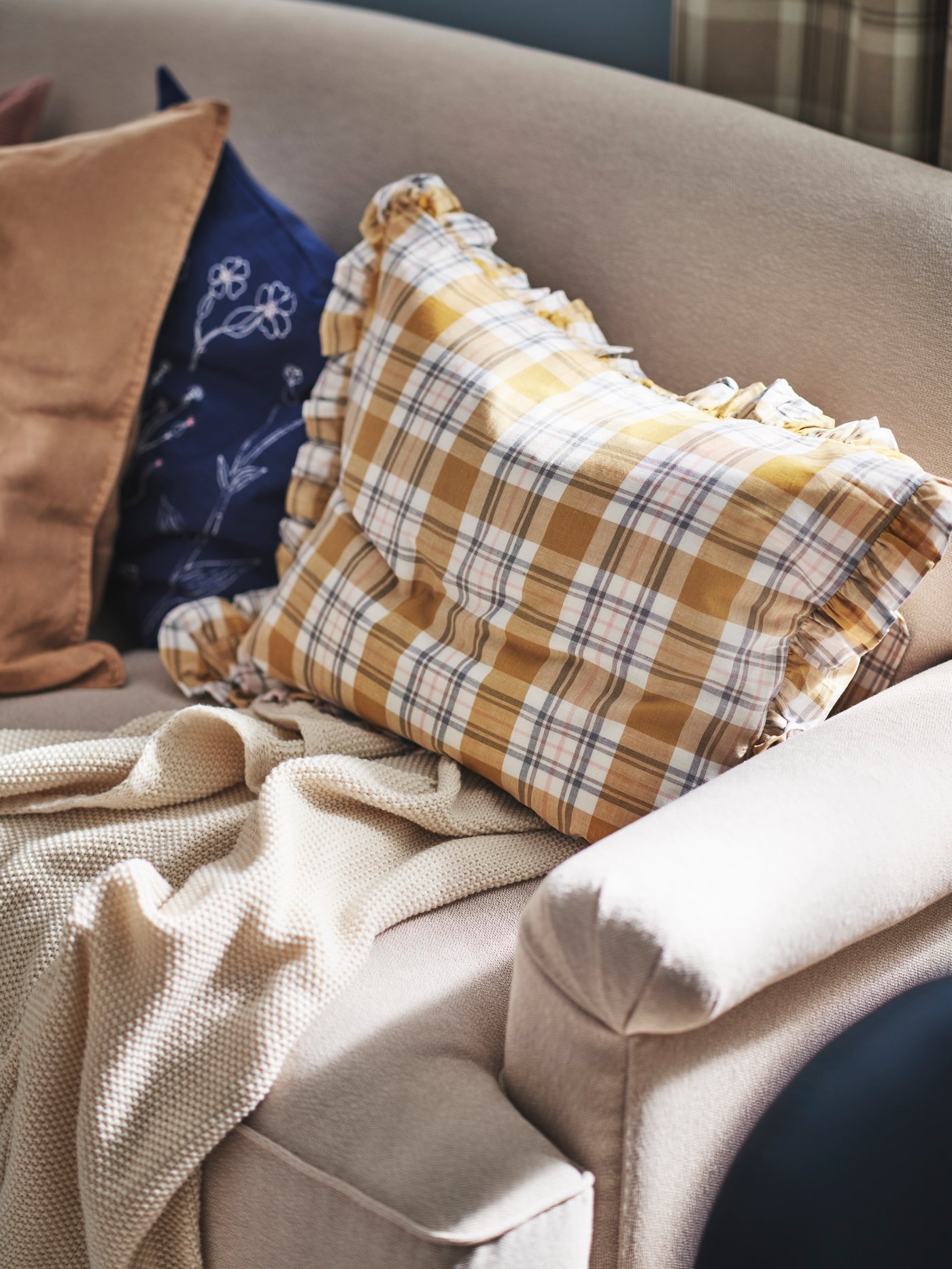 Salón con una funda de almohada PARKOLVON colocada sobre un sofá de 2 plazas ESSEBODA estándar junto a una funda de cojín ÅKERNEJLIKA azul.