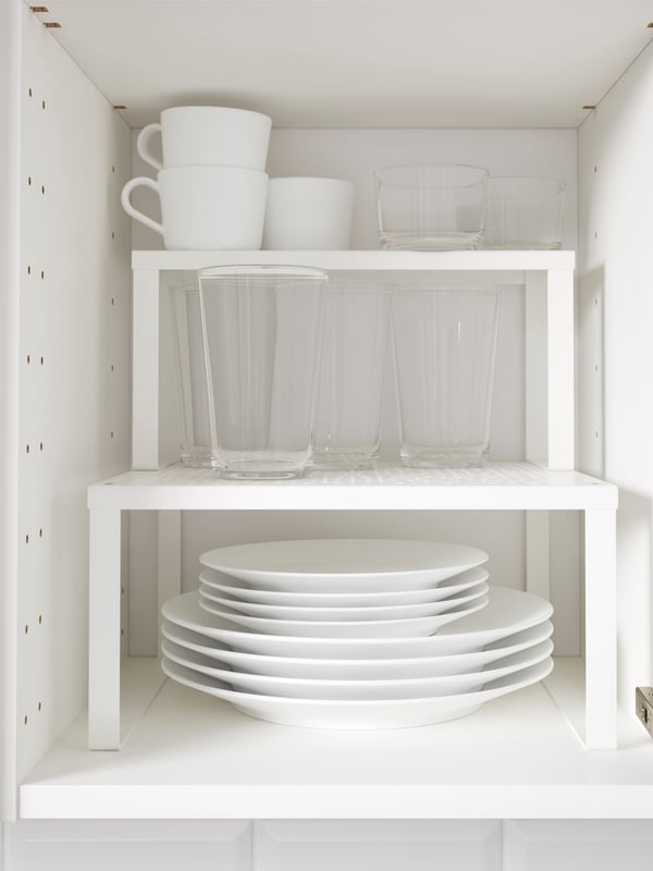 Interior de armario de cocina con dos estantes adicionales y platos y tazas.