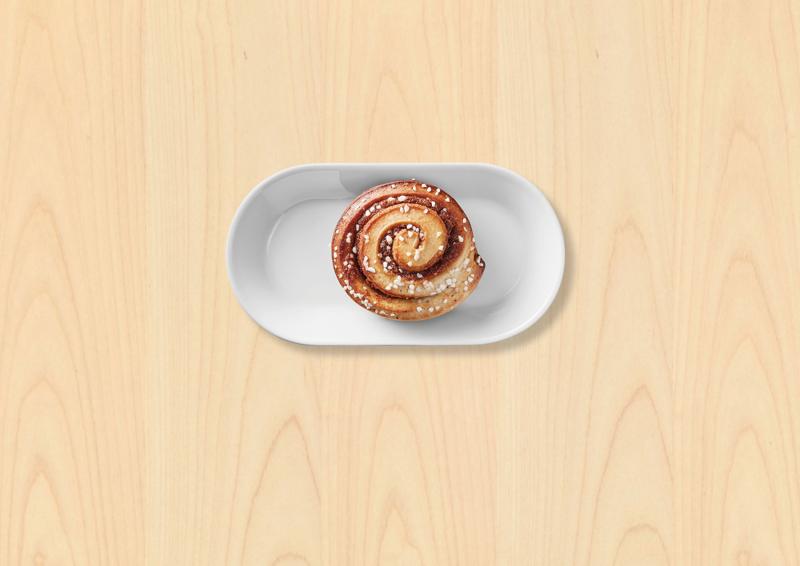 Un roulé à la canelle (KANELBULLAR) dans une assiette blanche sur fond bois