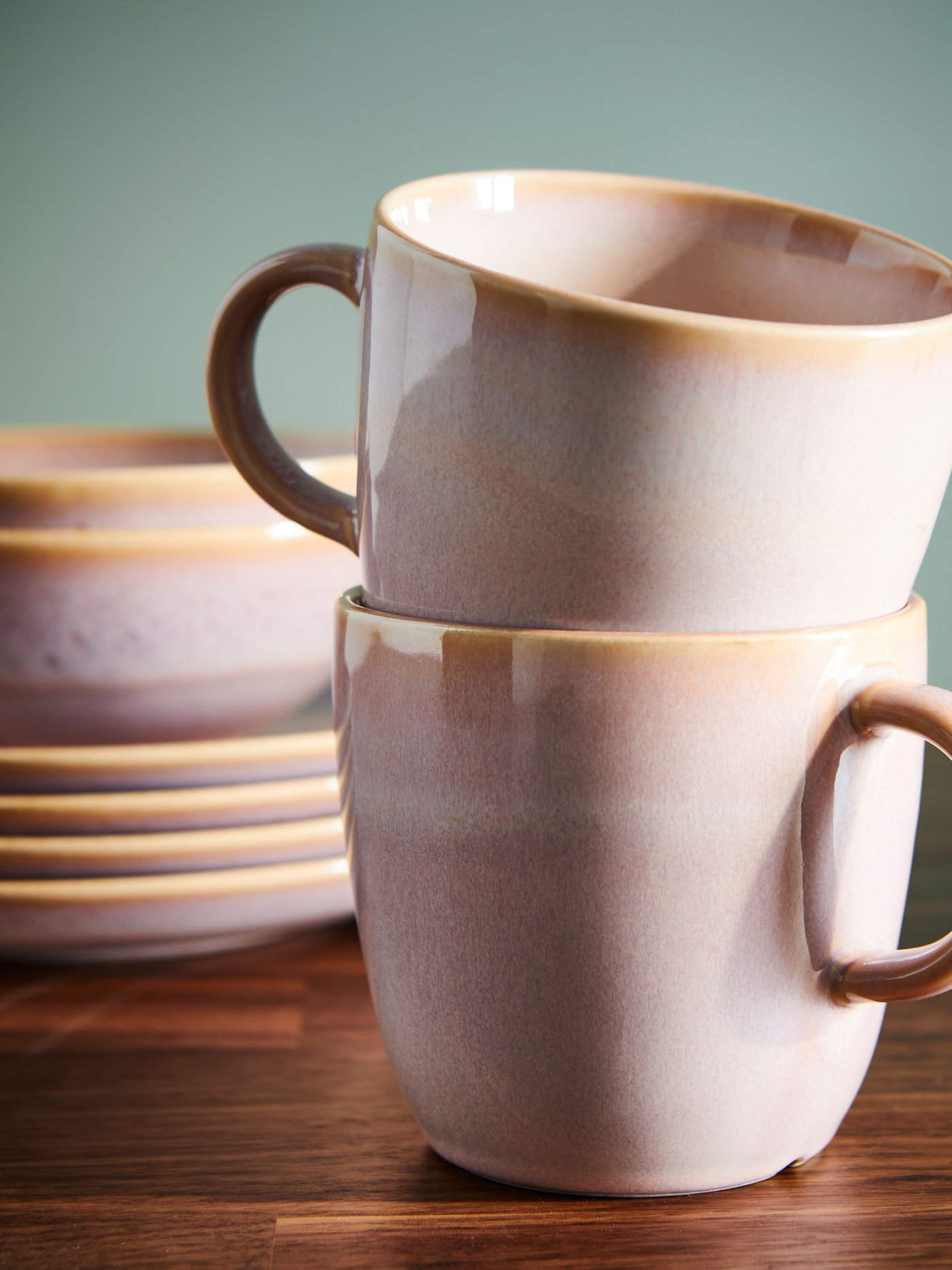 Stapel av keramikkoppar i mjuka pastellfärger på ett träbord.