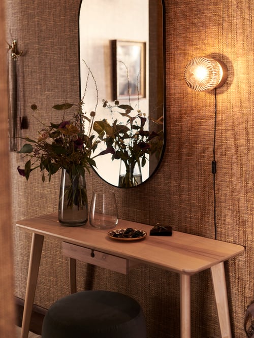 Traditional hallway area featuring a rectangular desk with two vases, and a lit wall lamp next to a mirror.