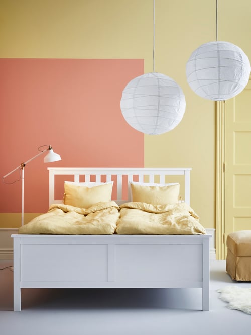 Bedroom with white wooden bed frame, yellow duvet cover and two pillowcases, white reading lamp, white pendant lamp shades.