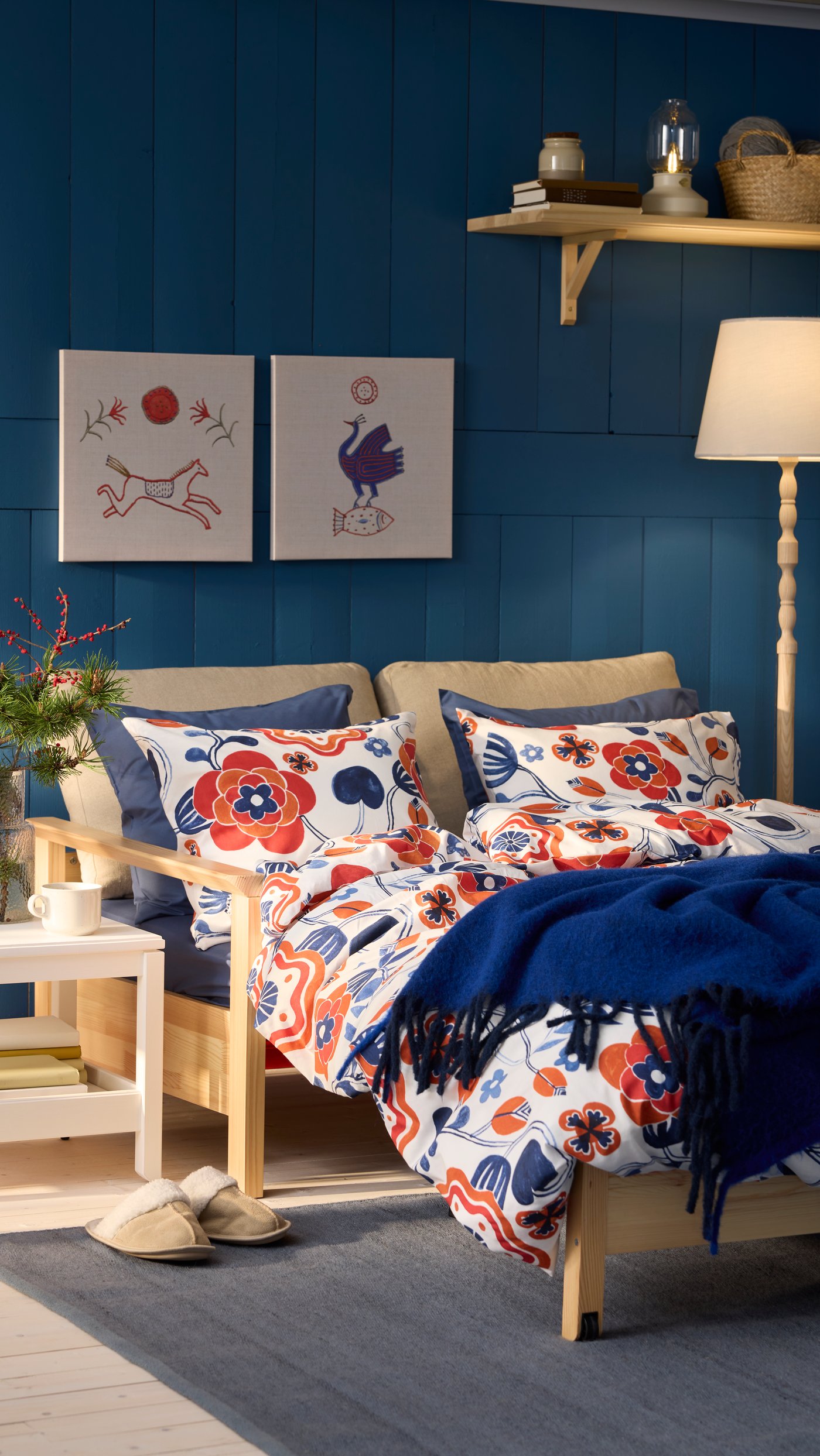 In einem Wohnzimmer steht ein Schlafsofa, auf dem geblümte Bettwäsche in rot blau liegt.