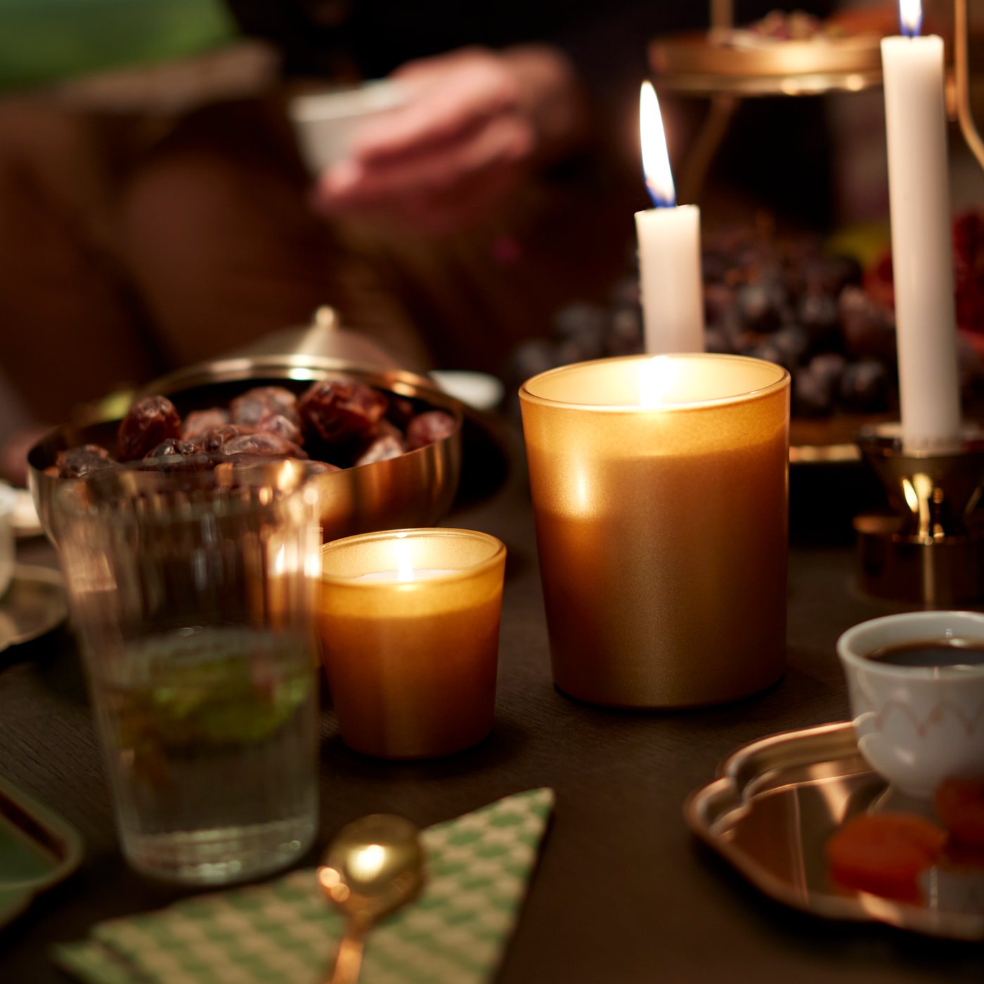 A glowing GOKVÄLLÅ scented candle in glass, sandalwood patchouli scent, in a cosy living room setting.