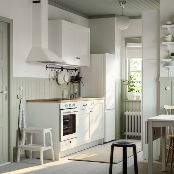 Petite cuisine en parallèle avec éléments bas et muraux KNOXHULT en blanc et barre support HULTARP où sont suspendus des accessoires de cuisine.