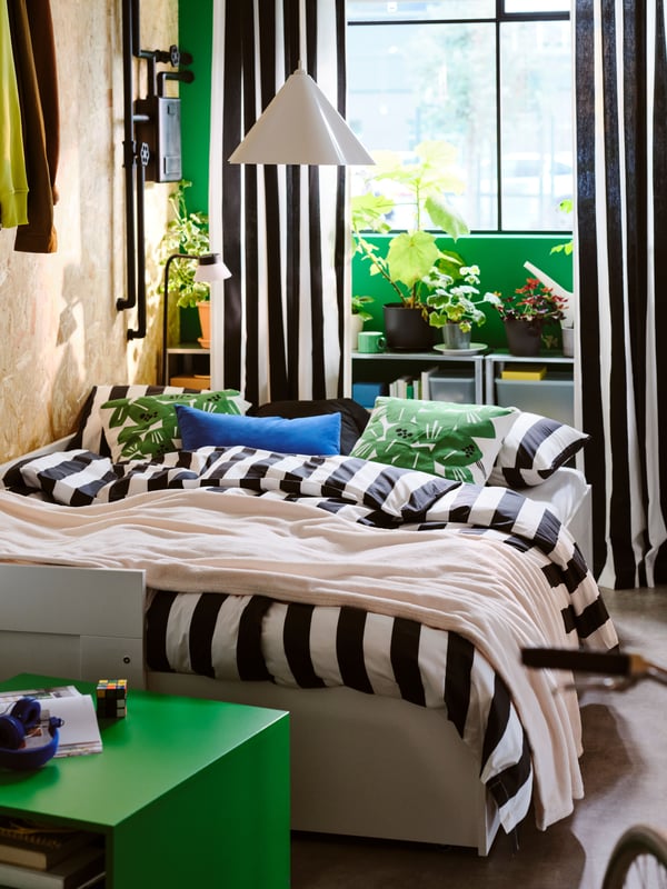 A white BRIMNES day-bed with 2 drawers opened as a double bed, with black/white striped SLÅNHÖSTMAL bed linen on top.