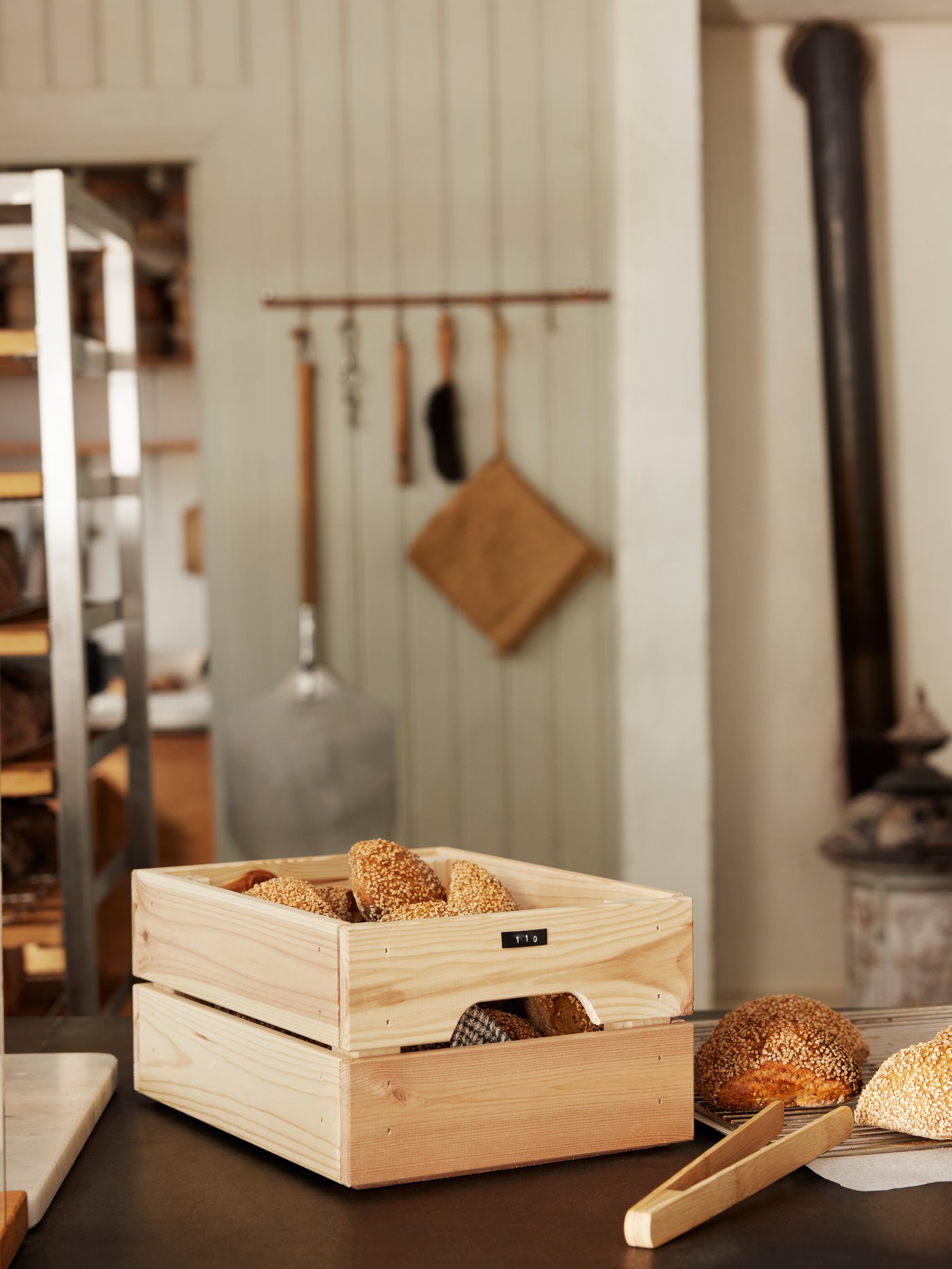 A pine KNAGGLIG box sits filled with bread on a kitchen counter. 