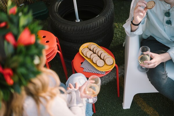 Persone che conversano con accanto sgabelli rossi MARIUS. Su uno di questi c'è un vassoio KOPPARBJÖRK con biscotti.
