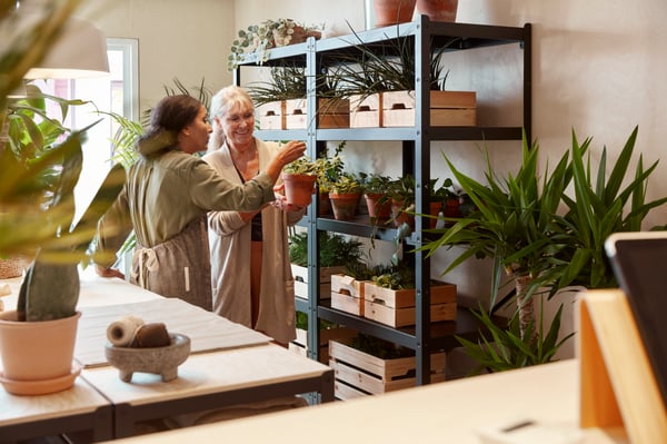 Two women point to plants in a BROR shelving unit