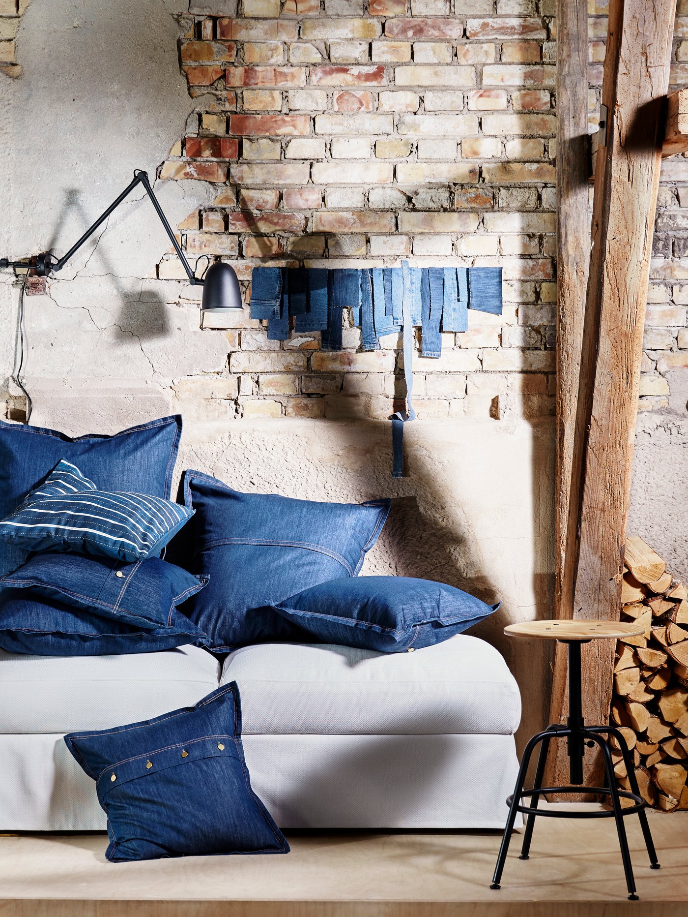 A lot of cushions in blue SISSIL cushion covers lie on top of two footstools against a wall in a run-down building.