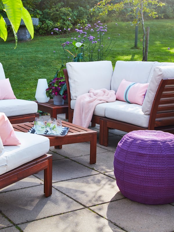 A 4-seat conversation set and a table in acacia wood, beige outdoor cushions, a purple pouffe and pink cushions.