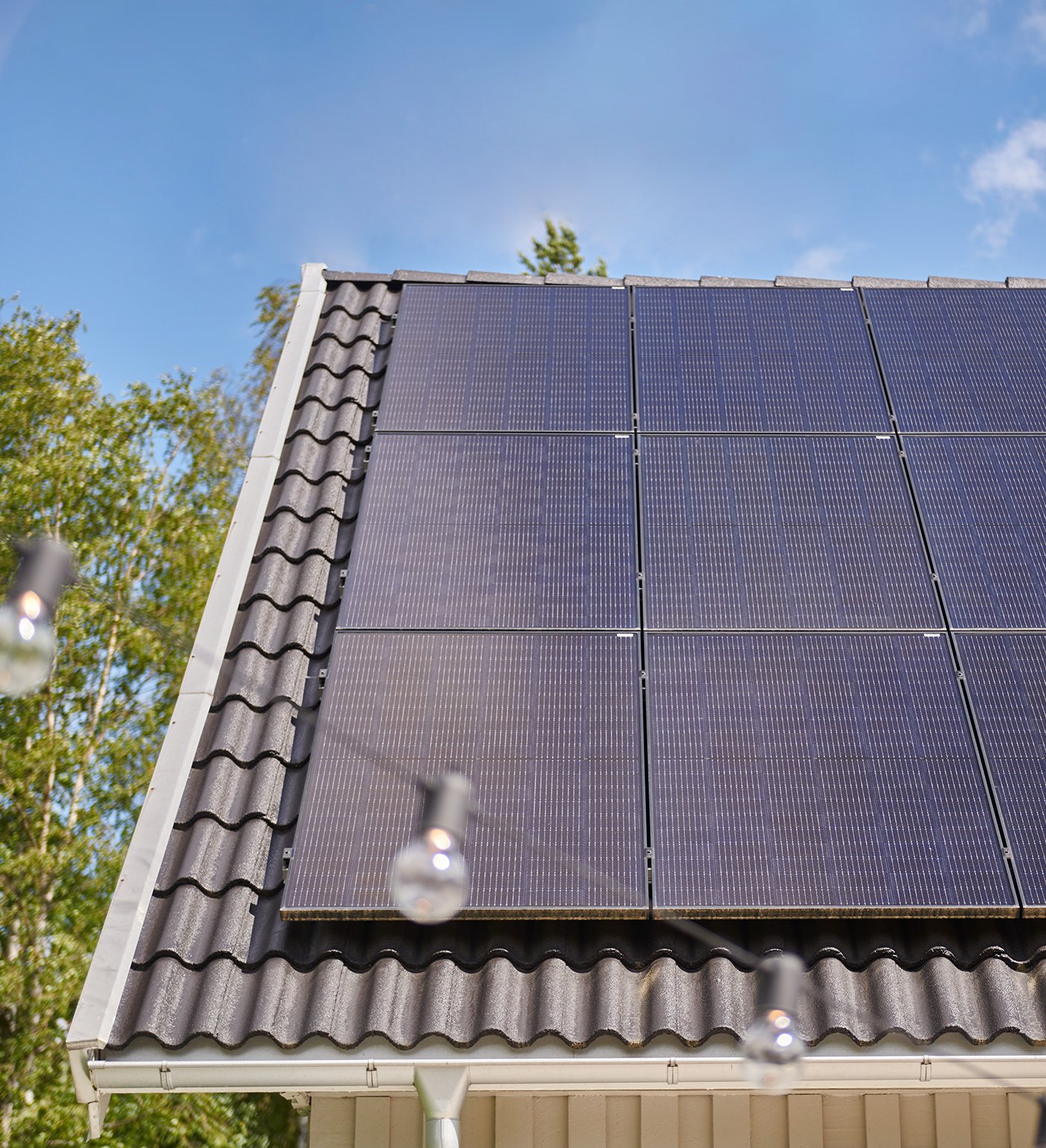 Solpaneler monterade på ett villatak med tegelprofiler, med blå himmel och träd i bakgrunden