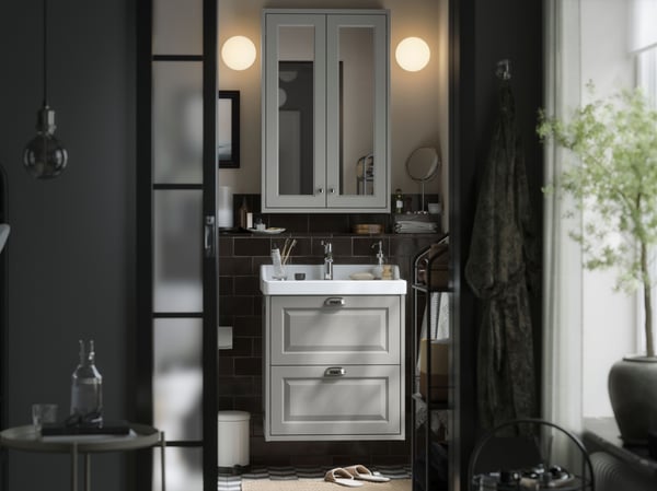 A small traditional style bathroom with white TÄNNFORSEN storage furniture, two soft round lamps and black details.