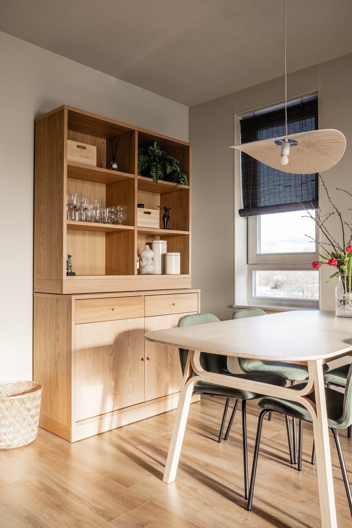 Een woonkamer met tegen de muur een TONSTAD opbergcombinatie in eikenfineer. Daarvoor staat een VOXLÖV eettafel in licht bamboe en 4 grijsgroene SKÅLSTA eettafelstoelen.