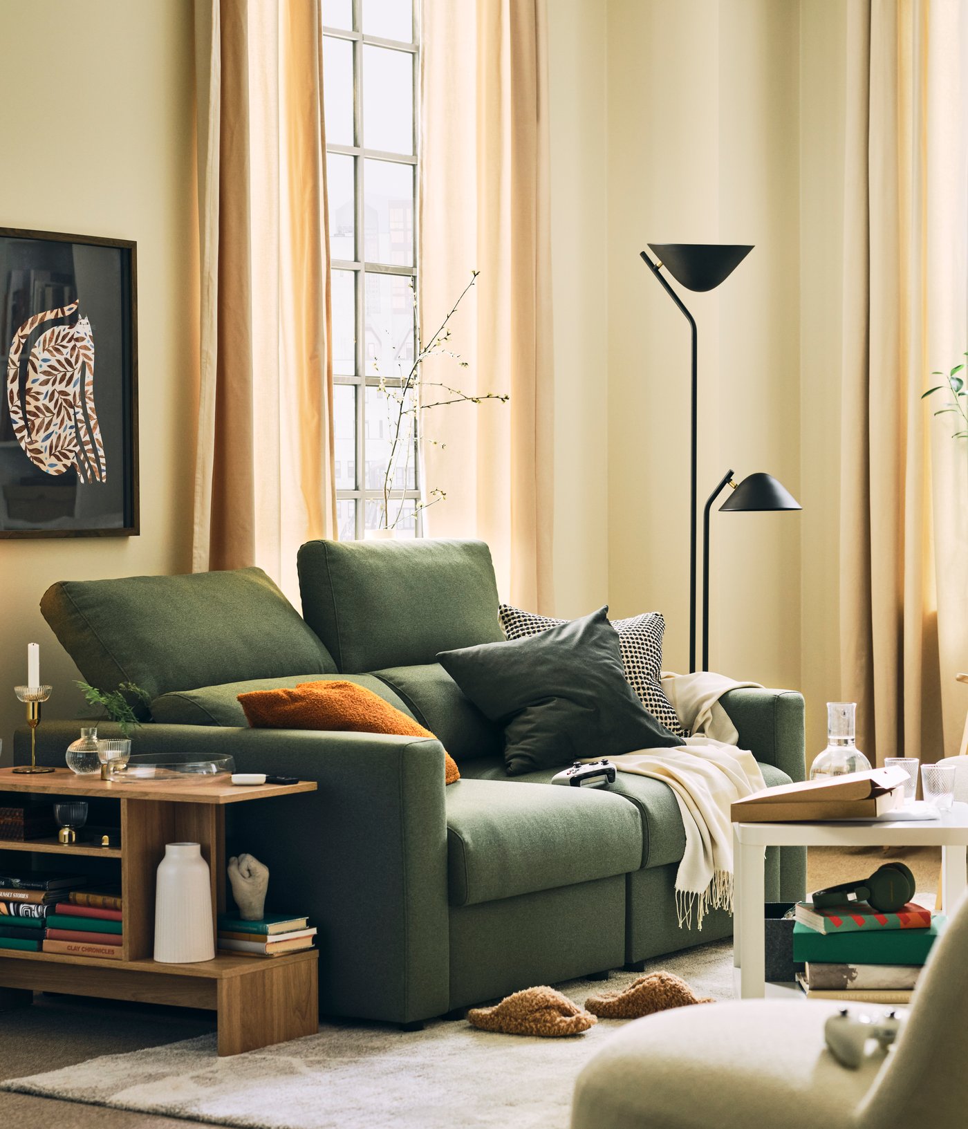 A light living room with a grey-green MALMKÖPING two-seat sofa flanked by a HOLMERUD side table, a floor lamp and plants.