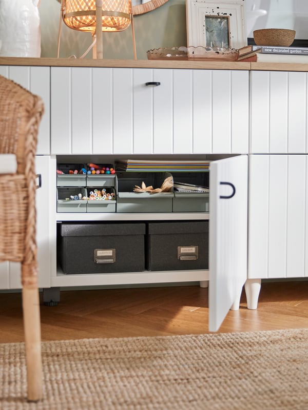 Traditional style BESTÅ unit with patterned white wood doors. Paper storage can be seen inside. 