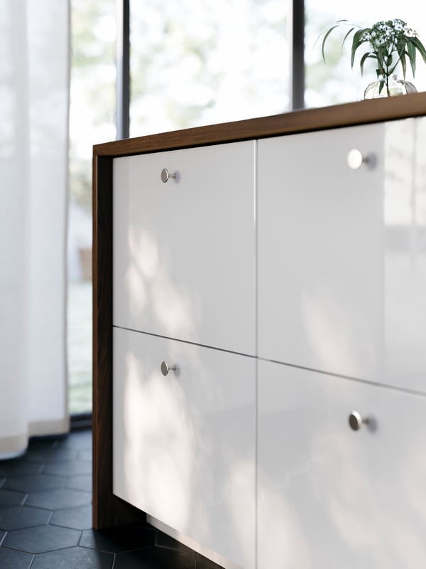 A large kitchen island has four drawers with high-gloss white RINGHULT fronts and KALERUM knobs in a stainless steel colour.