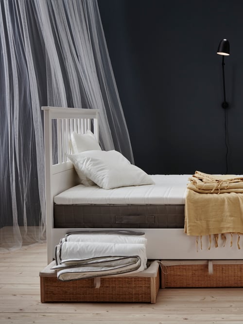 Schlafbereich mit einem HEMNES Bettgestell mit der HAMARVIK Federkernmatratze, LILL Gardinenschals und einem GULDPALM Kissen fest. Unter dem Bett sind Bettkästen zu sehen.