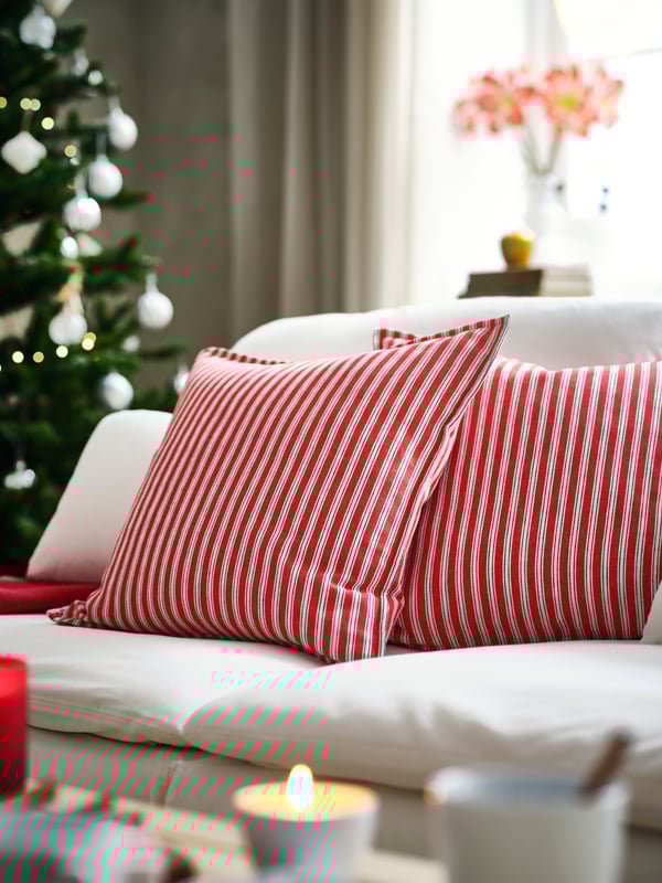 Wohnzimmer mit rot-weiß gestreiften Kissen, Kerzen und Weihnachtsbaum im Hintergrund