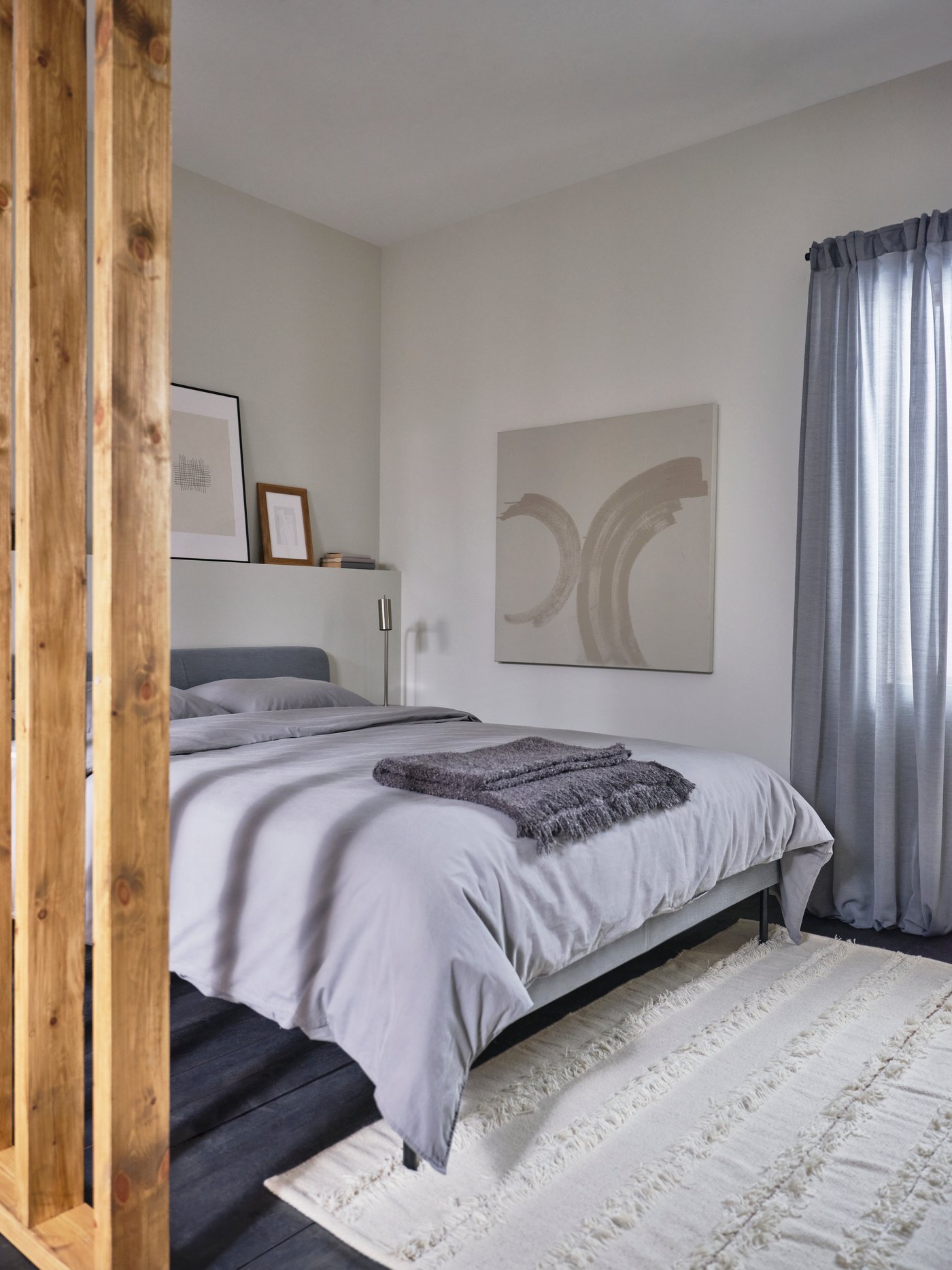 Una habitación de hotel con una cama doble. La cama tiene textiles en tonos grises, al igual que la cortina de la habitación.