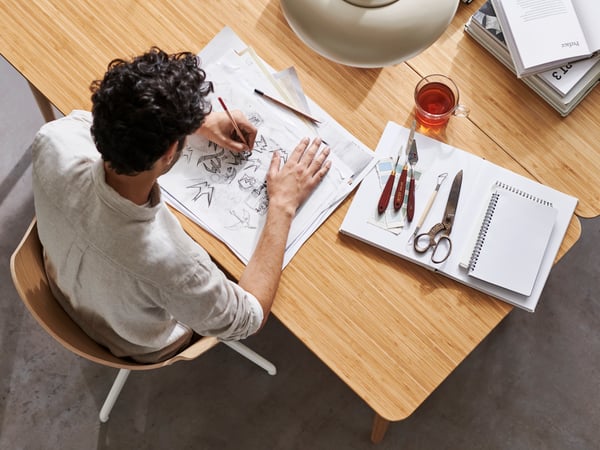 A man sits at an ANFALLARE / HILVER desk, creatively engaged in drawing.