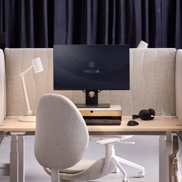 A desk setup with a beige MITTZON acoustic screen made from Gunnared fabric that separates two workspaces from each other.