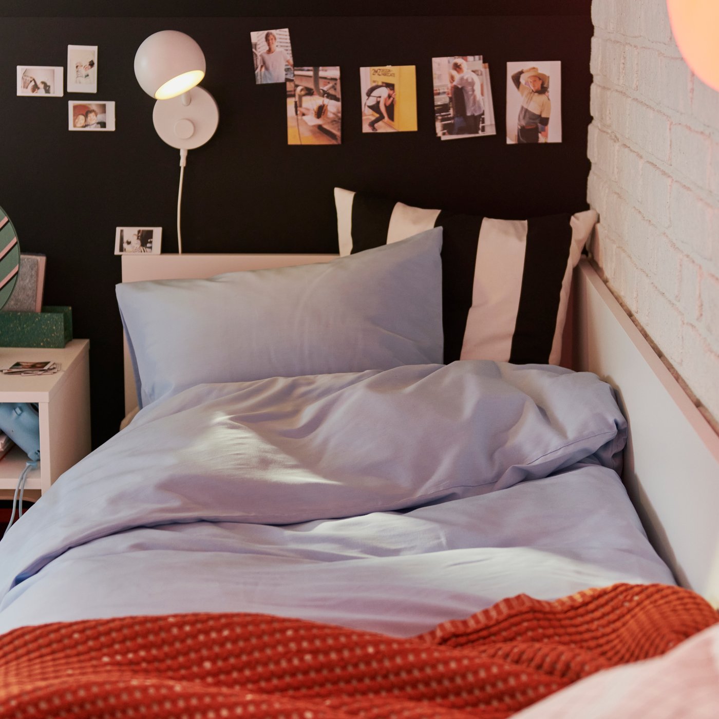 A single bed set against a dark wall features light blue PILTANDVINGE duvet cover and pillowcase and a warm-red blanket.