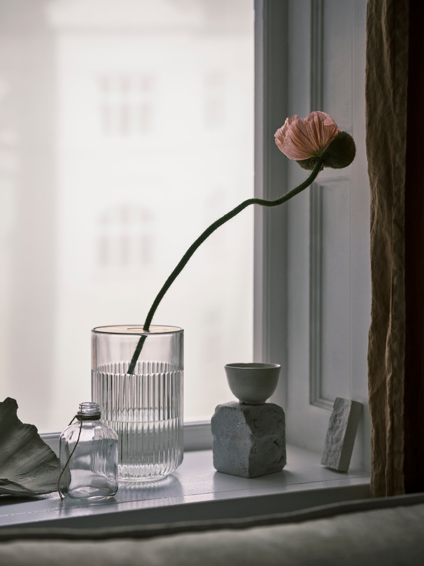 Lasinen maljakko ikkunalaudalla, maljakossa on yksi kukka.