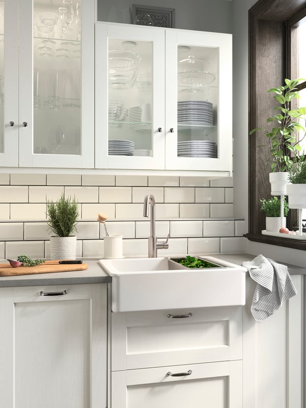 Une cuisine aux façades ENKÖPING blanches, un évier HAVSEN blanc, des rangements muraux et des cache-pots blancs où poussent des herbes vertes.