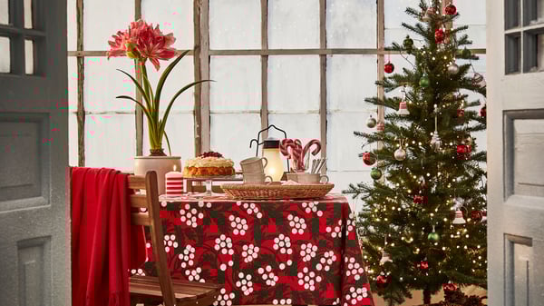 Afternoon tea / fika in greenhouse at Christmas time with red and white VINTERFINT tablecloth, artificial tree and LED lights.