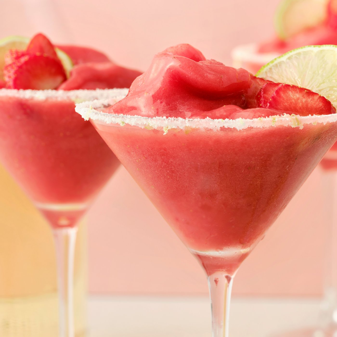 Two tall glasses filled with margaritas made of ISKUB elderflower soft drink and frozen strawberries, garnished with lime.