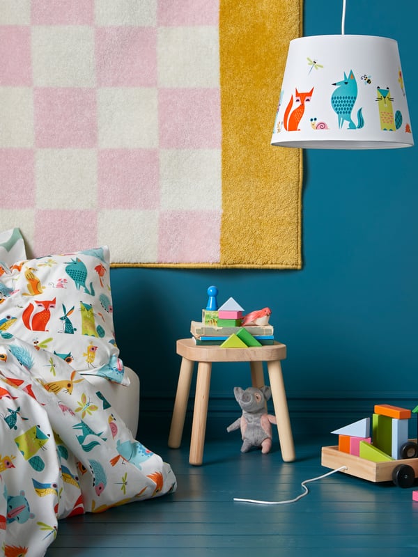 Two young girls relaxing in a bed made with a colourful green dotted quilt cover placed in a colourful children’s room.