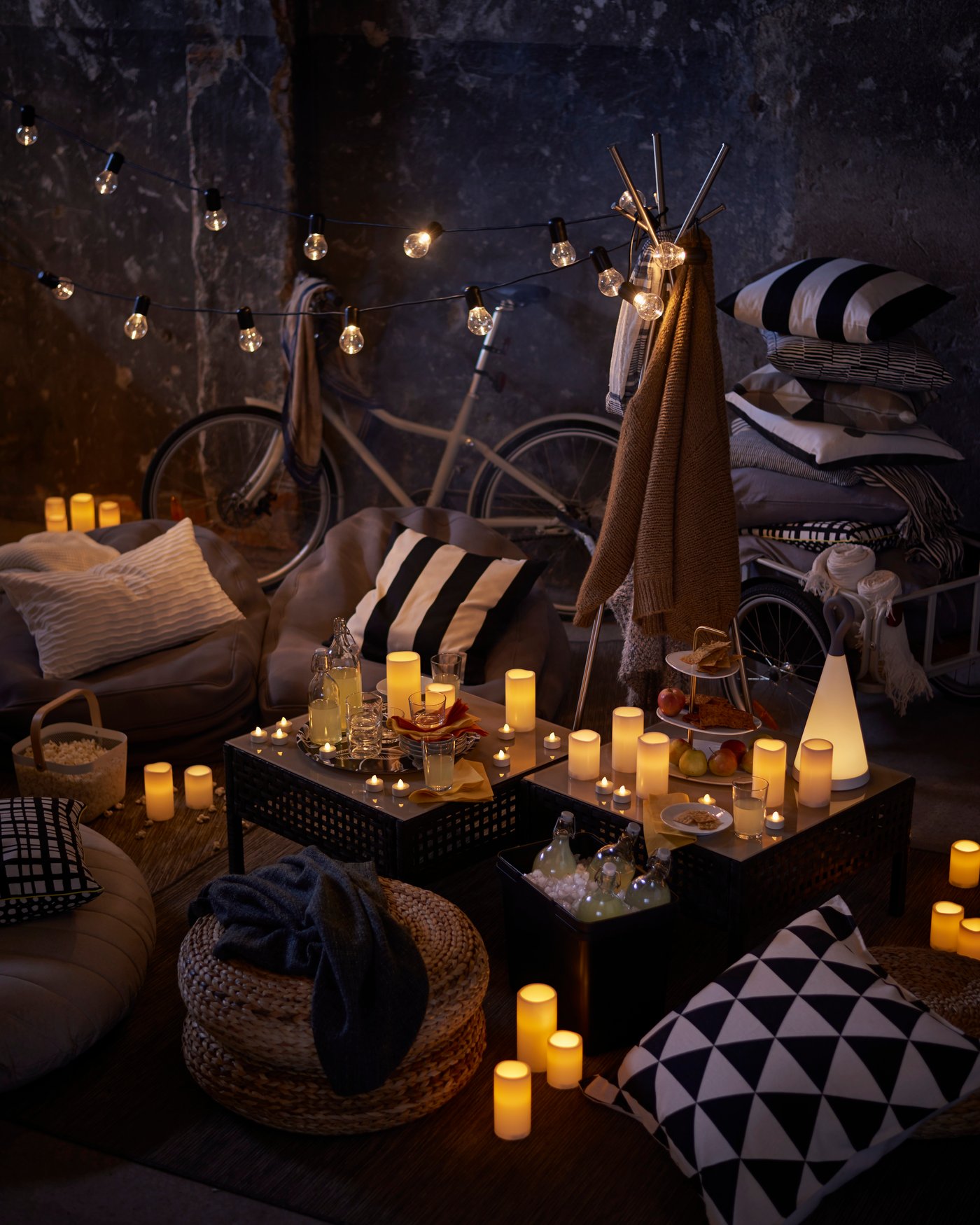 Two coffee tables set up with LED candles on top, various chairs and floor cushions around it, including a banana fibre ALSEDA stool outside.