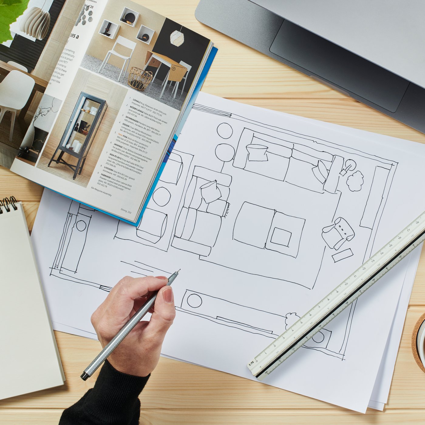 Půdorys a katalog IKEA, vedle nich je ruka držící tužku nad pracovním stolem s náčrtem uspořádání místnosti.