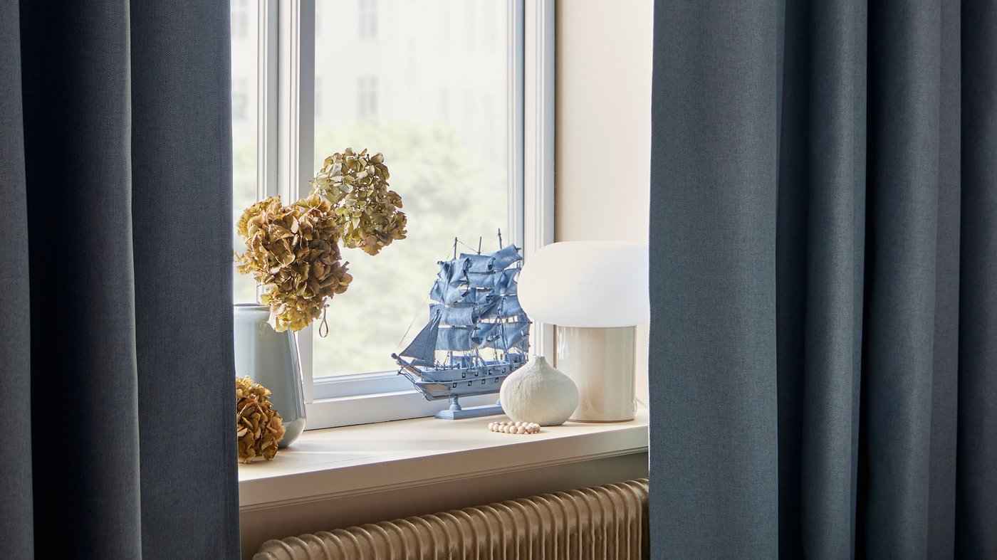 Fönster med blåa gardiner och en liten fönsterlampa. 