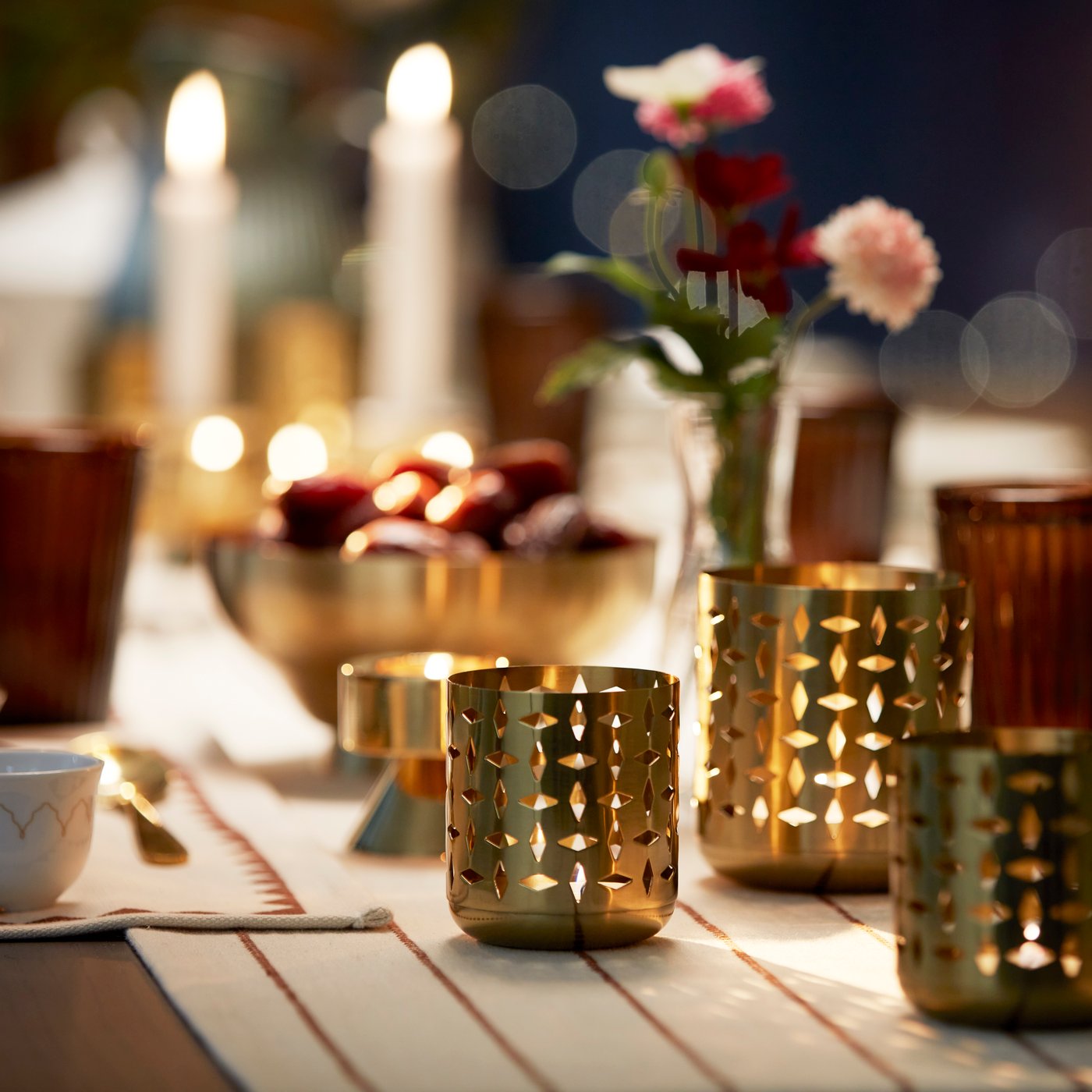 A close-up of some GOKVÄLLÅ tealight holders with lit candles, in a festive table setting.