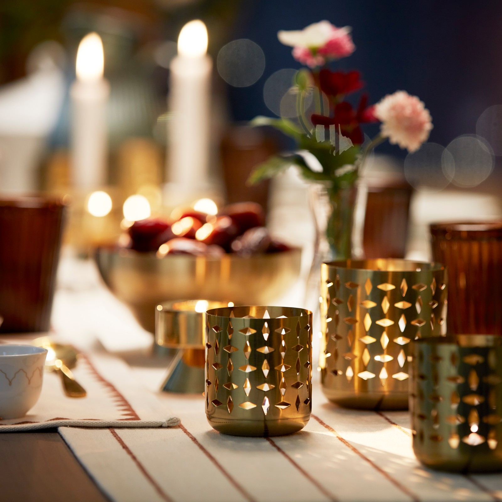 A close-up of some GOKVÄLLÅ tealight holders with lit candles, in a festive table setting.