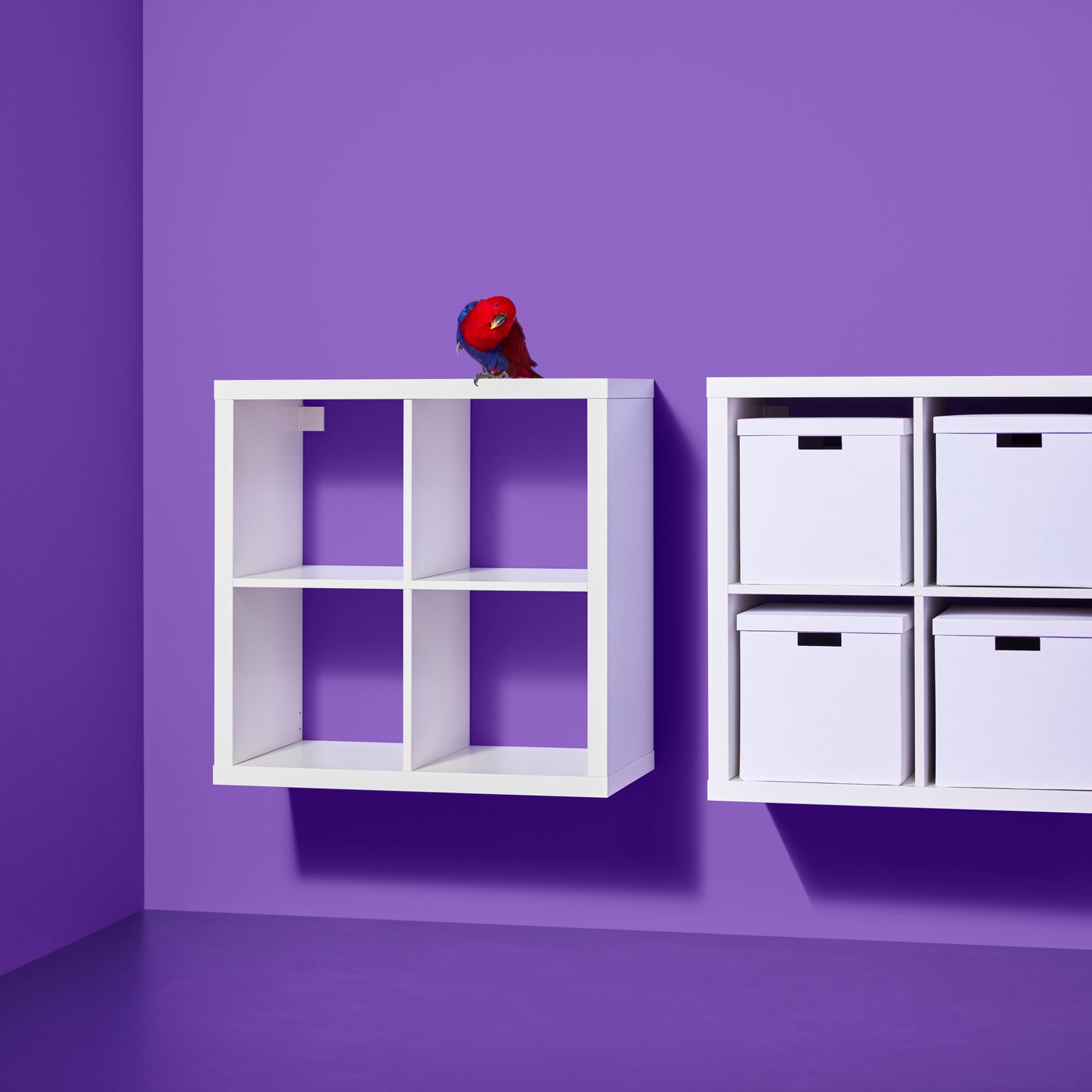 Två vita KALLAX hyllor hänger mot en lila vägg, en tom, och den andra med vita förvaringslådor på hyllorna.